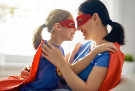 Mother and her child playing together. Girl and mom in Superhero costume. Mum and kid having fun, smiling and hugging. Family holiday and togetherness.の写真素材