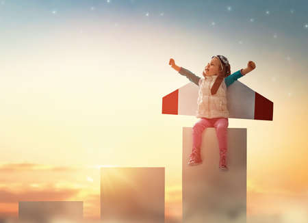 Little child playing pilot. Girl on the background of sunset sky. Kid in an astronaut costume...