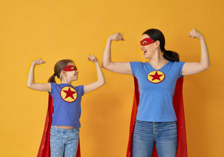 Mother and her child playing together. Girl and mom in Superhero costumes. Mum and kid having fun and smiling. Family holiday and togetherness.の写真素材