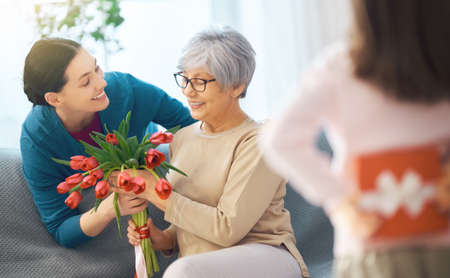 Happy women's day! Child daughter is congratulating mom and granny giving them flowers tulips....