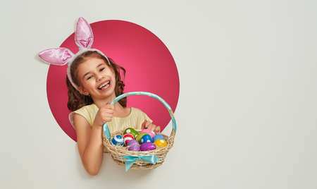 Cute little child wearing bunny ears on Easter day. Girl with painted eggs on pink and white...