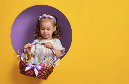 Cute little child on Easter day. Girl with painted eggs on bright purple and yellow background.