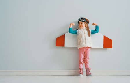 Little child girl in an astronaut costume is playing and dreaming of becoming a spaceman. Portrait of funny kid on a background of grey wall.の写真素材