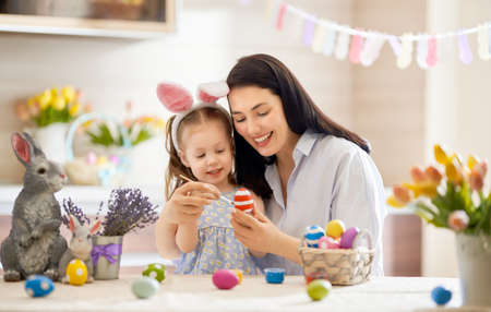 Happy holiday! A mother and her daughter are painting eggs. Family preparing for Easter. Cute little...