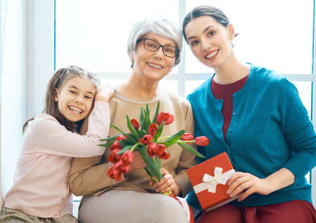 Happy women's day! Child daughter is congratulating mom and granny giving them flowers tulips....