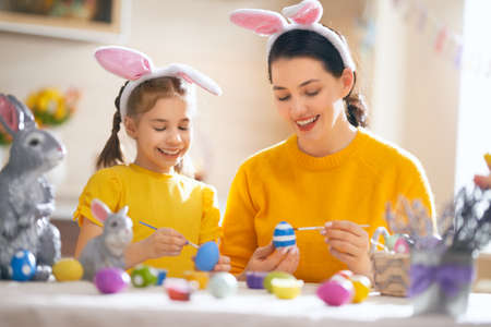 Happy holiday! A mother and her daughter are painting eggs. Family preparing for Easter. Cute little...