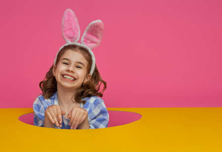 Cute little child wearing bunny ears on Easter day. Girl with painted eggs on bright pink and yellow...