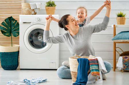 Beautiful young woman and child girl little helper are having fun and smiling while doing laundry at home.の写真素材