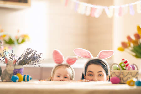 Happy holiday! A mother and her daughter are painting eggs. Family preparing for Easter. Cute little child girl is wearing bunny ears.の写真素材