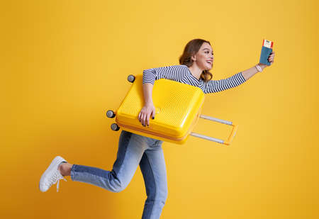 Go on an adventure! Happy woman going traveling. Young person with suitcase on color yellow background.の写真素材