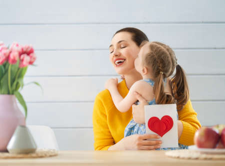 Happy mother's day! Child daughter is congratulating mom and giving her card. Mum and girl smiling. Family holiday and togetherness.の写真素材