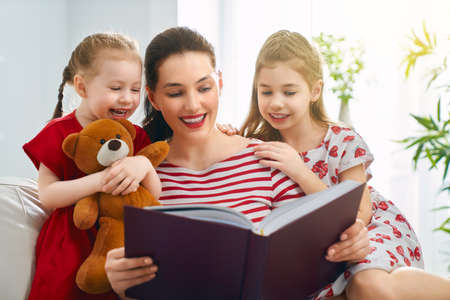 happy loving family. pretty young mother reading a book to her daughtersの写真素材