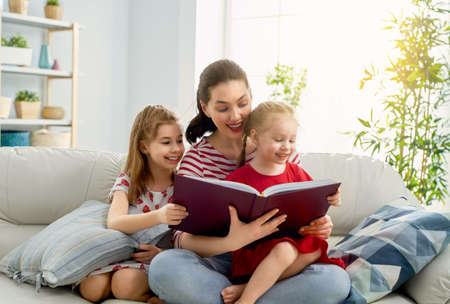 happy loving family. pretty young mother reading a book to her daughtersの写真素材