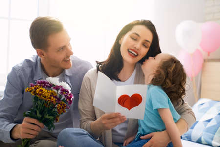 Happy mother's day! Children daughters with dad congratulating mom and give her flowers, gift and card. Family holiday and togetherness.の写真素材