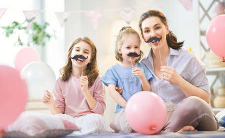 Funny time. Mom and her children daughters are playing at home. Cute girls are holding paper...