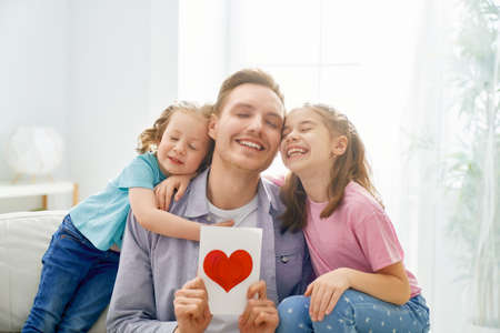 Happy father's day! Children daughters congratulating dad and giving him postcard. Daddy and girls...