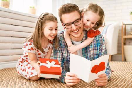 Happy father's day! Children daughters congratulating dad and giving him gift box. Daddy and girls smiling and hugging. Family holiday and togetherness.の写真素材