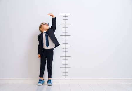 Little child is playing businessman. Kid is measuring the growth on the background of wall. Smart power concept.の写真素材
