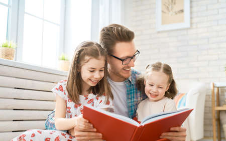 Happy loving family. Young father reading a book to his daughters.の写真素材