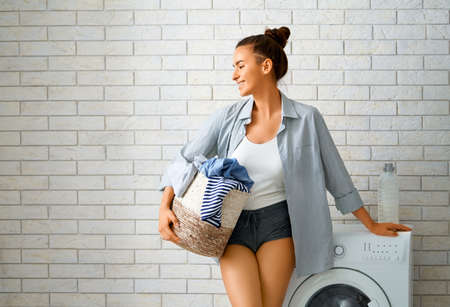 Beautiful young woman is smiling while doing laundry at home.の写真素材