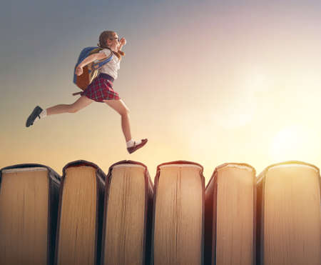 Back to school! Happy cute industrious child are running on books on sunset landscape.の写真素材