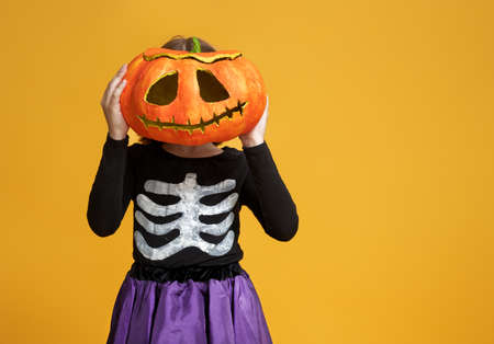 Happy Halloween! Cute little girl in skeleton costume with pumpkin on yellowの写真素材