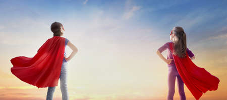 Little children are playing superhero. Kids on the background of sunset sky. Girl power concept