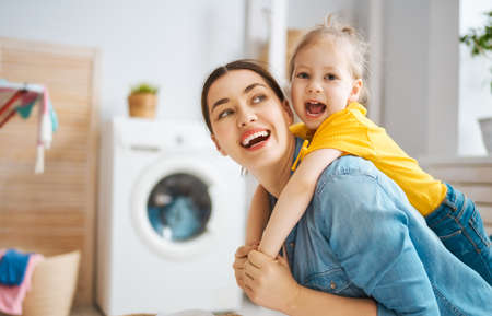 Beautiful young woman and child girl little helper are having fun and smiling while doing laundry at home.の写真素材