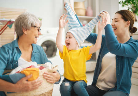 grandma, mom and child are doing laundry at home. three generations of familyの写真素材