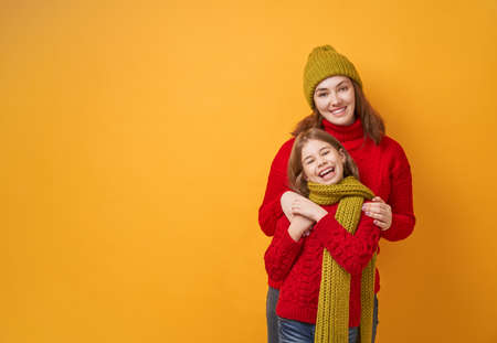 Winter portrait of happy loving family wearing knitted hats, snoods and sweaters. Mother and child girl having fun, playing and laughing on yellow background. Fashion concept.の写真素材