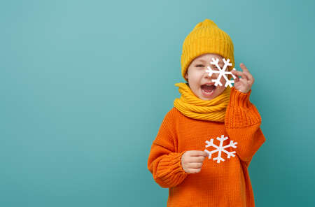 Winter portrait of happy child wearing knitted hat, snood and sweater. Girl having fun, playing and laughing on teal background. Fashion concept.の写真素材