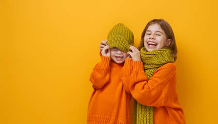 Winter portrait of happy children wearing knitted hat, snood and sweaters. Girls having fun, playing and laughing on yellow background. Fashion concept.の写真素材