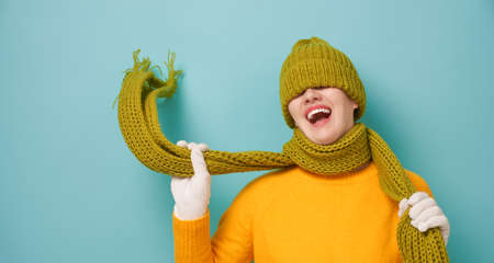 Winter portrait of happy young woman wearing knitted hat, scarf and sweater. Girl having fun on bright teal background. Fashion concept.                                の写真素材