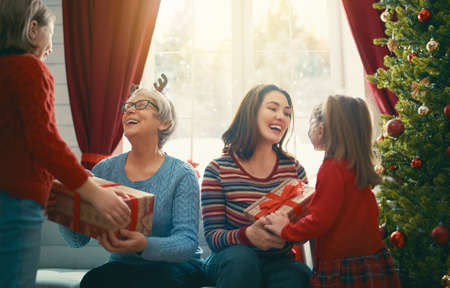 Merry Christmas and Happy Holidays! Cheerful kids presenting gifts to mom and granny. Parents and...