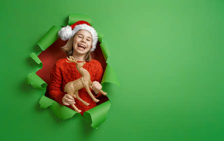 Merry Christmas! Little girl in Santa's hat on bright color background. Red and green.