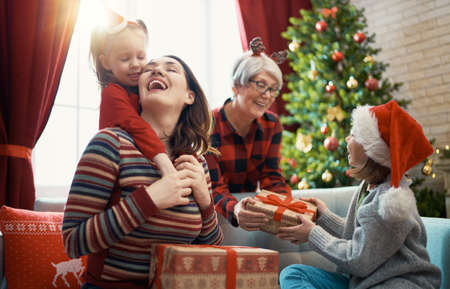 Merry Christmas and Happy Holidays! Cheerful kids presenting gifts to mom and granny. Parents and little children having fun near tree indoors. Loving family with presents in room.の写真素材