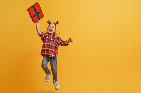 Happy little girl with Christmas gift on bright color background. Red and yellow.