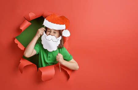 Merry Christmas! Little girl in Santa's hat on bright color background. Red and green.の写真素材