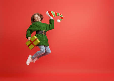 Happy little girl with Christmas gift on bright color background. Red and green.