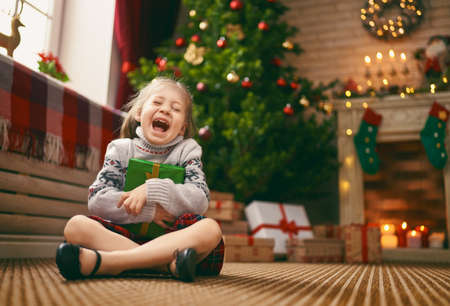 Merry Christmas and Happy Holidays! Cheerful cute child girl with gift. Kid is having fun near tree.の写真素材