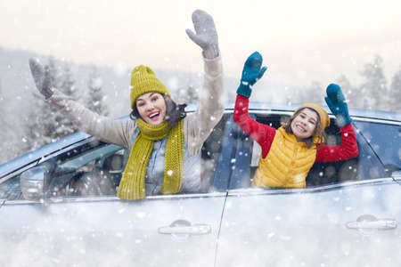 Toward adventure! Happy family are relaxing and enjoying road trip. Mother, child and car on snowy...