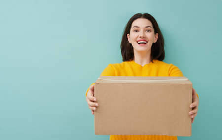 Beautiful young woman is holding cardboard box on turquoise background.