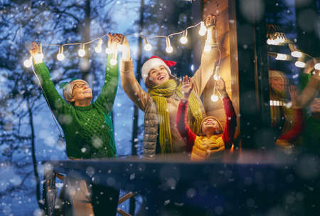 Merry Christmas and Happy Holidays! Cheerful mom, granny and cute girl decorating home. Parents and little child having fun outdoors. Loving family with garlands outside.の写真素材