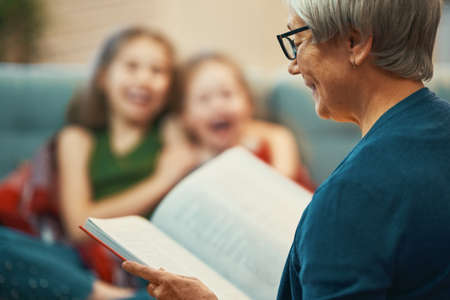 Grandmother reading a book to her granddaughters. Family holiday and togetherness.の写真素材