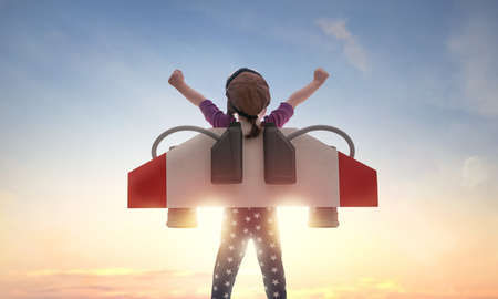 Little child playing pilot. Girl on the background of sunset sky. Kid in an astronaut costume...