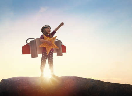 Little child playing pilot. Girl on the background of sunset sky. Kid in an astronaut costume dreaming of becoming a spaceman.の写真素材