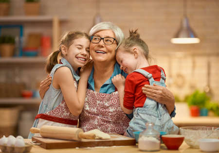 Happy loving family are preparing bakery together. Granny and children are cooking cookies and having fun in the kitchen. Homemade food and little helper.の写真素材