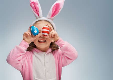 Cute little child wearing bunny ears on Easter day. Girl with painted eggs on grey background.の写真素材