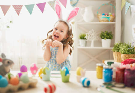 Beautiful child painting eggs. Happy family preparing for Easter. Cute little girl is wearing bunny ears.の写真素材