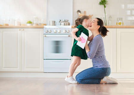 Happy mother's day! Child daughter is congratulating mom and giving her postcard. Mum and girl smiling and hugging. Family holiday and togetherness.